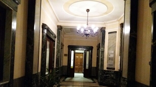 Ein Korridor mit Marmorboden, einem Chandelier und einer Holztür am Ende.