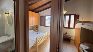 Un dormitorio con cama de madera, una mesita de noche, ventana con vistas y un baño con lavabo y espejo.