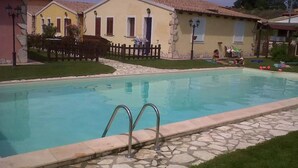 Una piscina con baldosas de piedra y barandillas metálicas, rodeada de césped y una valla de madera.