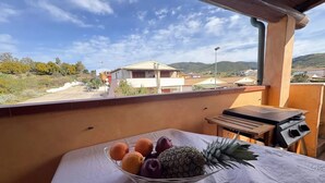 Un balcón con mesa, una parrilla y una cesta de fruta.