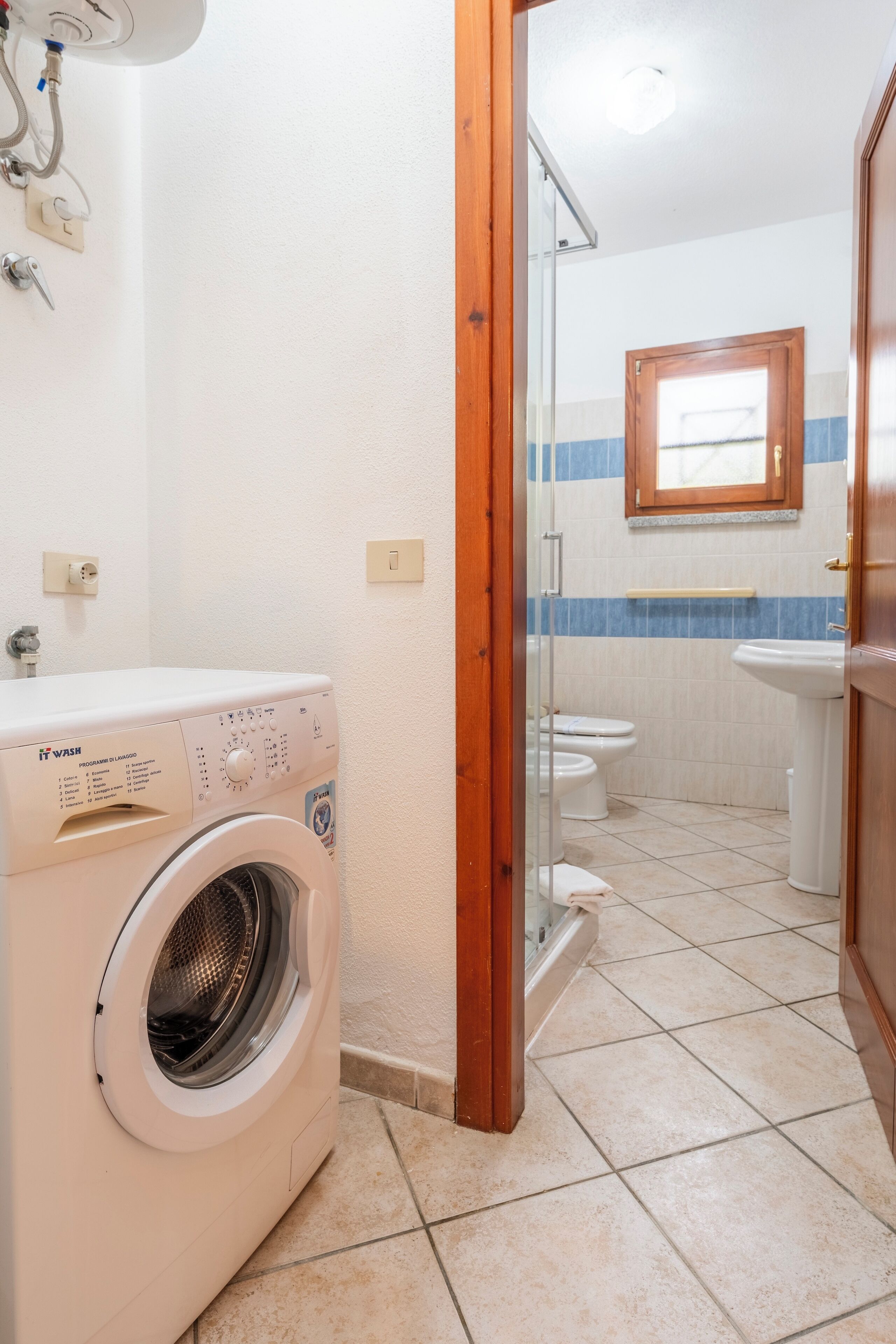 Un angolo lavanderia con lavatrice, cabina doccia in vetro e bagno con WC e lavandino.