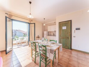 A dining area with a table set for four, a kitchen with white cabinets, and a sliding glass door leading to an outdoor balcony. - Modern house in Santa Teresa Gallura (Santa Teresa Gallura)
