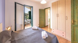 Quarto com cama, mesa de cabeceira, luminária, guarda-roupa e porta que dá para uma varanda.