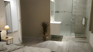 Een moderne badkamer met een douchecabine van glas, een witte wastafel en een potplant.