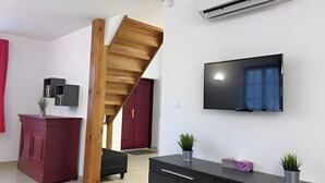 Een moderne woonkamer met een houten trap, een flatscreen televisie, een rode kast en een zwarte bank.