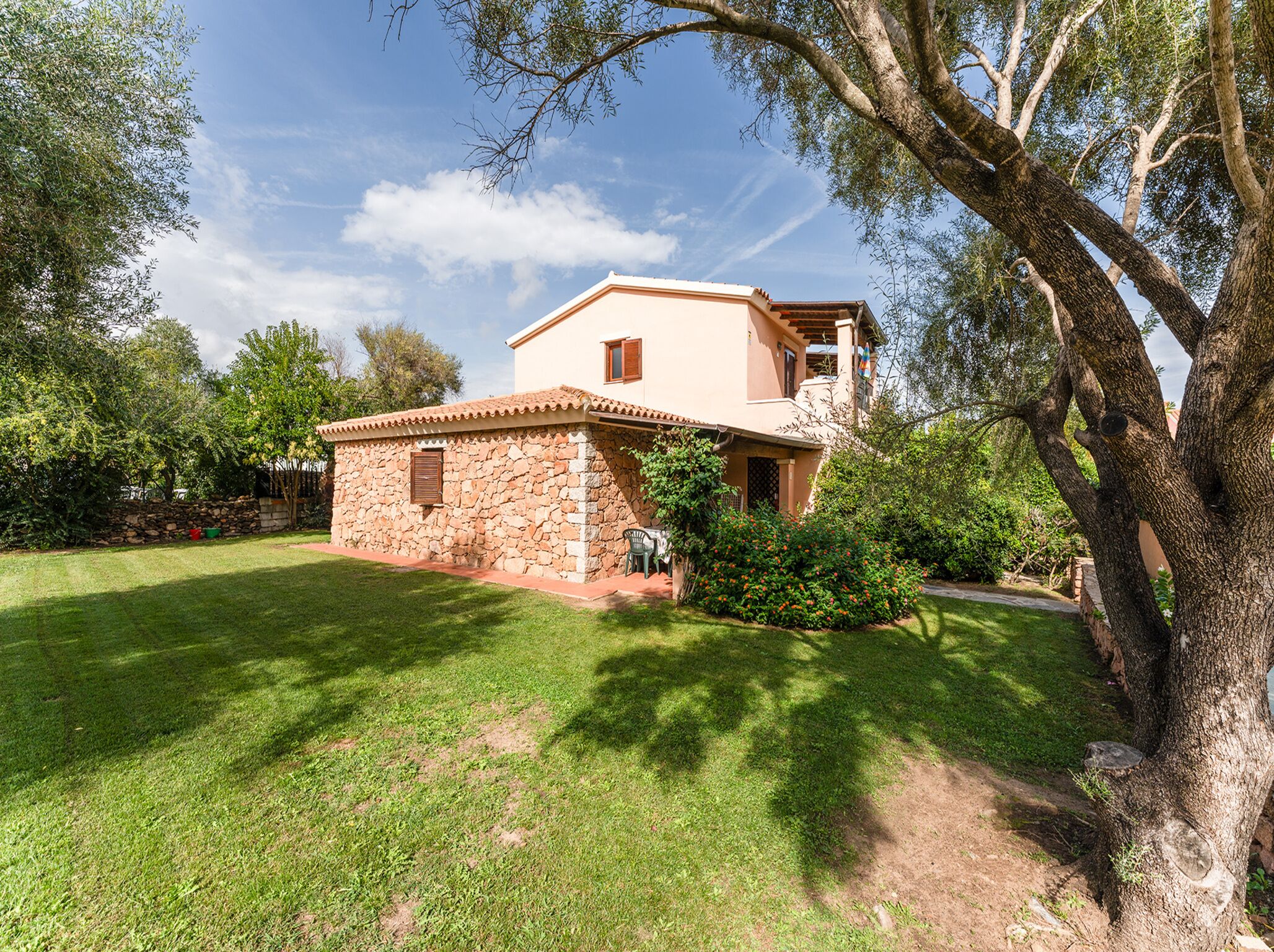A two-story house with a stone foundation and a tiled roof, surrounded by a well-maintained lawn and trees.