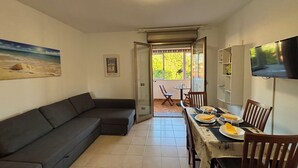 Een gezellige woonkamer met een bank, een eettafel gedekt voor twee personen en een aan de muur bevestigde televisie.