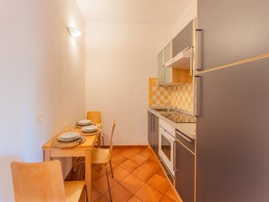 A compact kitchen with a dining table set for two, a refrigerator, oven, and a microwave. - Bright 3 guest apartment with pool (Santa Teresa Gallura)