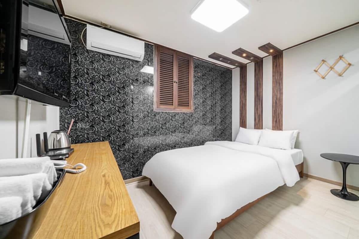 A modern hotel room with a bed, a wooden desk, a small table, and a TV.