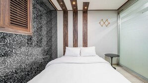 A modern bedroom with a large bed, a wooden slat vent, a patterned wall, and a small round table. - Hotel Hue (Incheon)