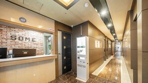 A hotel reception area with a 'SOME' sign, a reception desk, a CCTV sign, and a self-service kiosk. - Hotel Hue (Incheon)