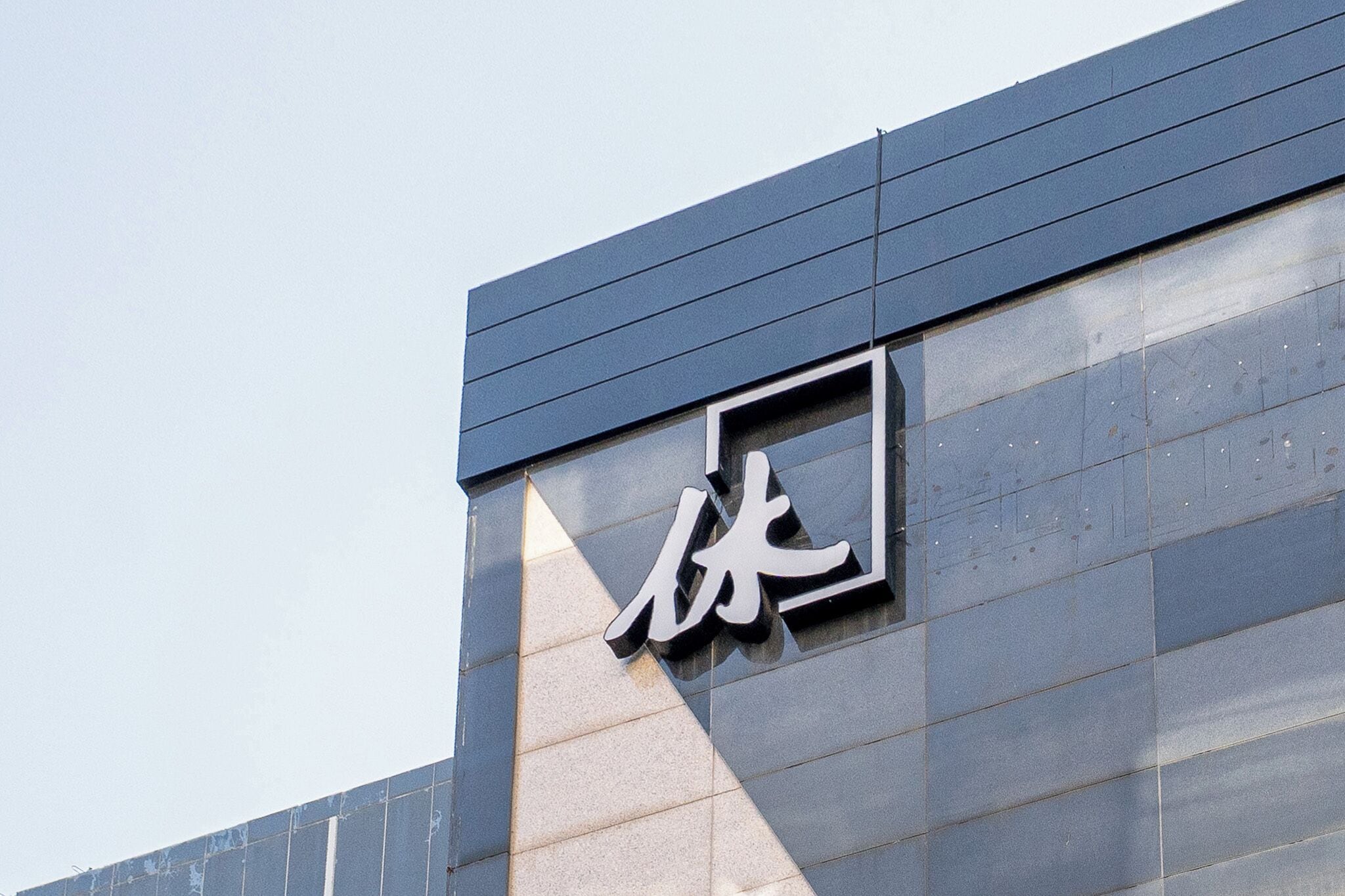 La façade d’un immeuble est ornée d’une grande enseigne moderne sur laquelle figurent des caractères chinois.