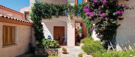 Un patio con un sendero de piedra, una puerta de madera y un pequeño espacio de estar con una mesa y sillas.