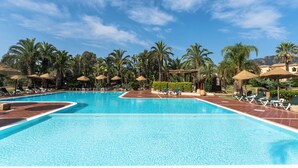 Une grande piscine extérieure dotée de plusieurs couloirs, entourée de palmiers et de chaises longues.
