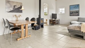 A modern living room with a wooden dining table, chairs, a fireplace, a television, and a sofa. - "Gjuro" - 400m from the sea by Interhome (Hjørring)