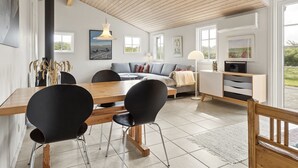 A modern living room with a wooden ceiling, a dining area with a wooden table and black chairs, a sofa with cushions, and a TV on a white cabinet. - "Gjuro" - 400m from the sea by Interhome (Hjørring)