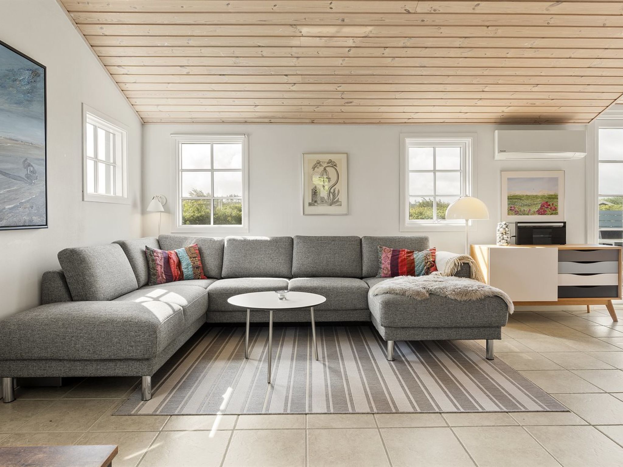 Een moderne woonkamer met een grijze modulaire bank, een ronde salontafel en een gestreept vloerkleed.