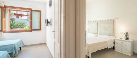 A bedroom with a bed, bedside table, and a window with a view of a building and greenery.