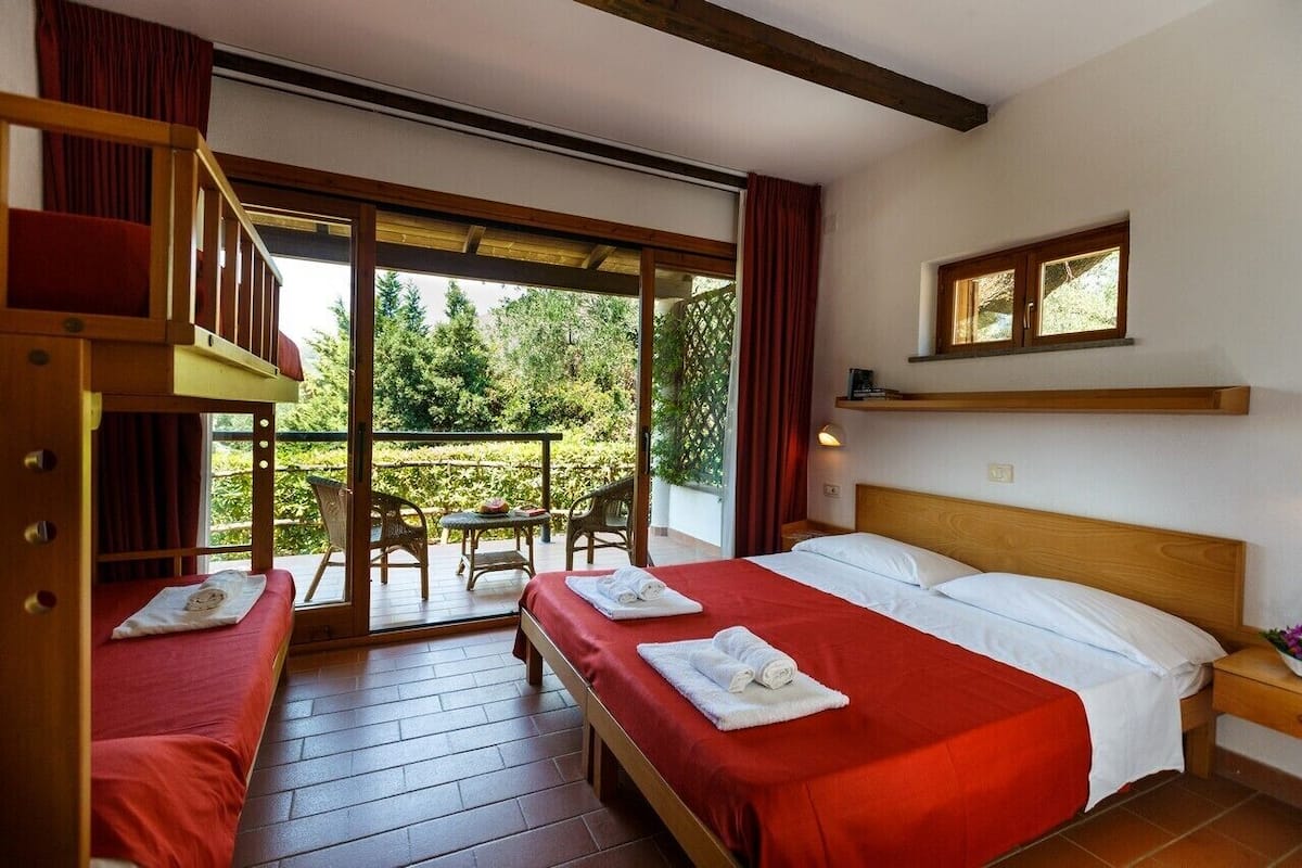 A room with two beds, a wooden headboard, a window, and a balcony with outdoor furniture.