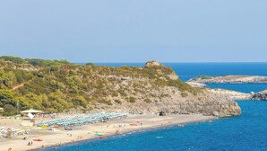 Una playa costera con afloramientos rocosos, cielo despejado y una vista distante del mar.