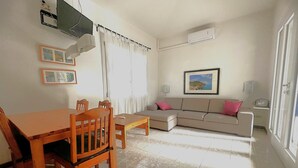 Ein Wohnzimmer mit Esstisch, Stühlen, einer Couch, einem Fernseher und einem gerahmten Bild an der Wand.
