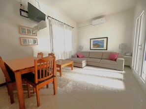 Ein Wohnzimmer mit Esstisch, Stühlen, einer Couch, einem Fernseher und einem gerahmten Bild an der Wand.