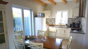 Una cucina con mobili bianchi, un tavolo di legno e sedie. Si nota un frigorifero, un lavello e una finestra con vista su un giardino.