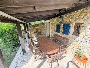 Eine Terrasse im Freien mit einem Holztisch und Bänken, Steinmauern und einem Steinboden.