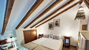 Ein Schlafzimmer mit einem großen Bett, Holzbalken, einem Schreibtisch und einer Hängelampe.