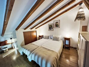 A bedroom with a large bed, wooden beams, a desk, and a hanging light fixture. - GITE im Herzen der Drôme Provençale by Interhome (La Begude de Mazenc)