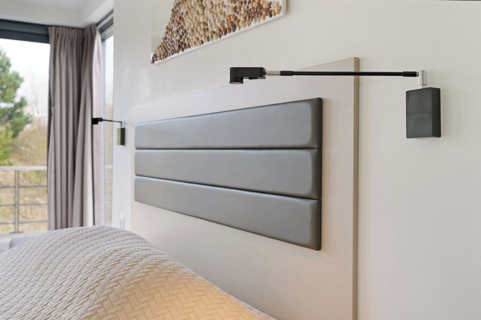 A modern bedroom with a large bed, a headboard with horizontal panels, and a wall-mounted light fixture.