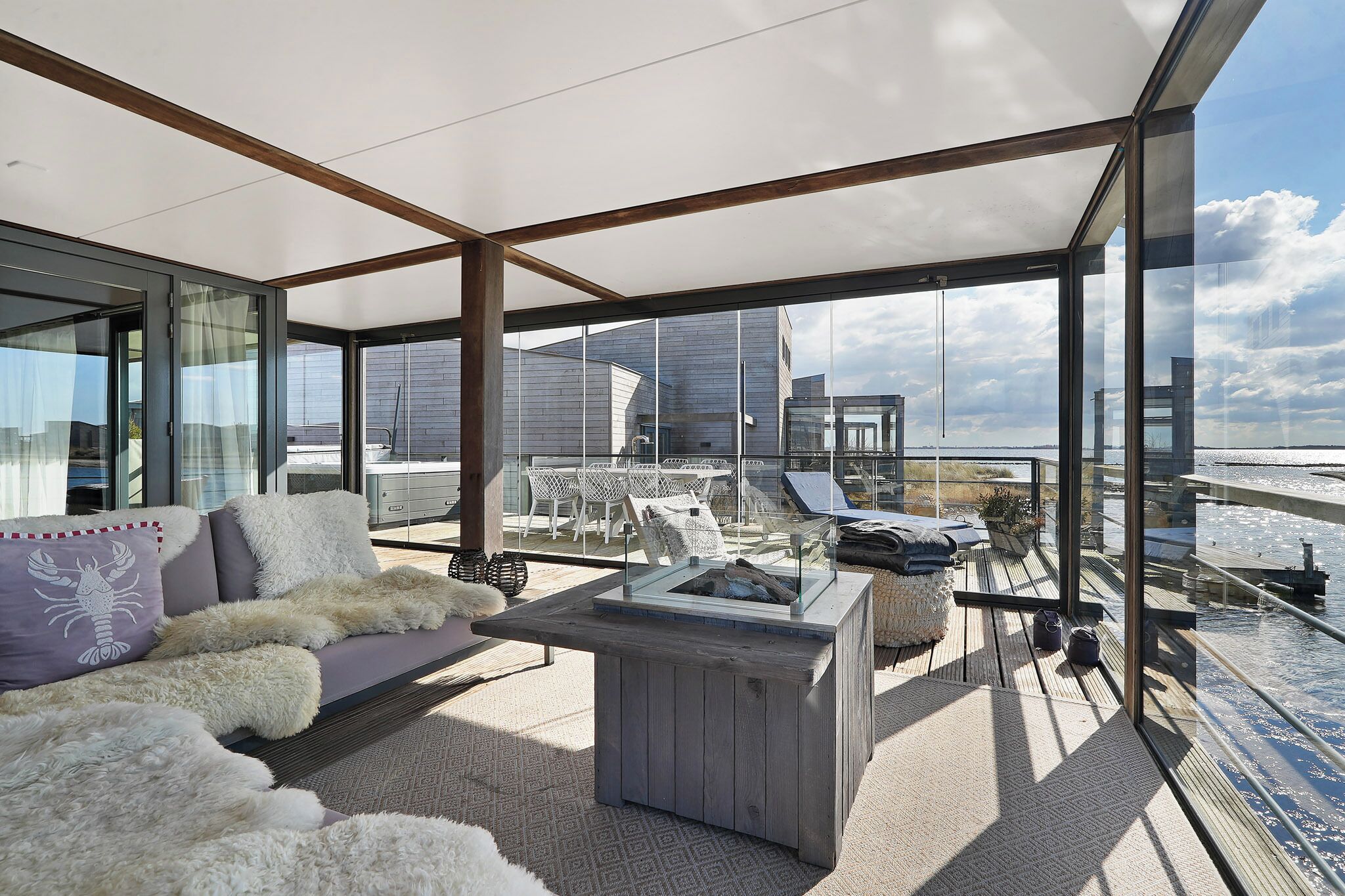 Un espacio exterior moderno con un sofá, una mesa de madera y un cerramiento de vidrio.