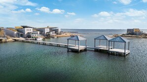 A waterfront property with a dock extending into the water, featuring a modern house and two gazebos. - The terraces of a 4-person Villa Super VIP are located directly by the water, with access to a private swimming pier, jacuzzi and Infrared sauna. (Ouddorp)