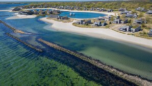 An aerial view of a coastal residential area with houses and a beach. - The 4-person Villa Super VIP features a luxurious and comfortably furnished interior with a direct waterfront location, various terraces offering unobstructed views over the water. (Ouddorp)