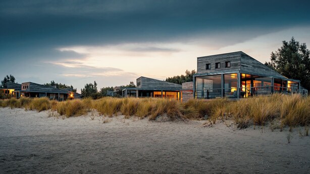 A modern beach house with large windows and a wooden exterior. - The 4-person Villa Super VIP features a luxurious and comfortably furnished interior with a direct waterfront location, various terraces offering unobstructed views over the water. (Ouddorp)