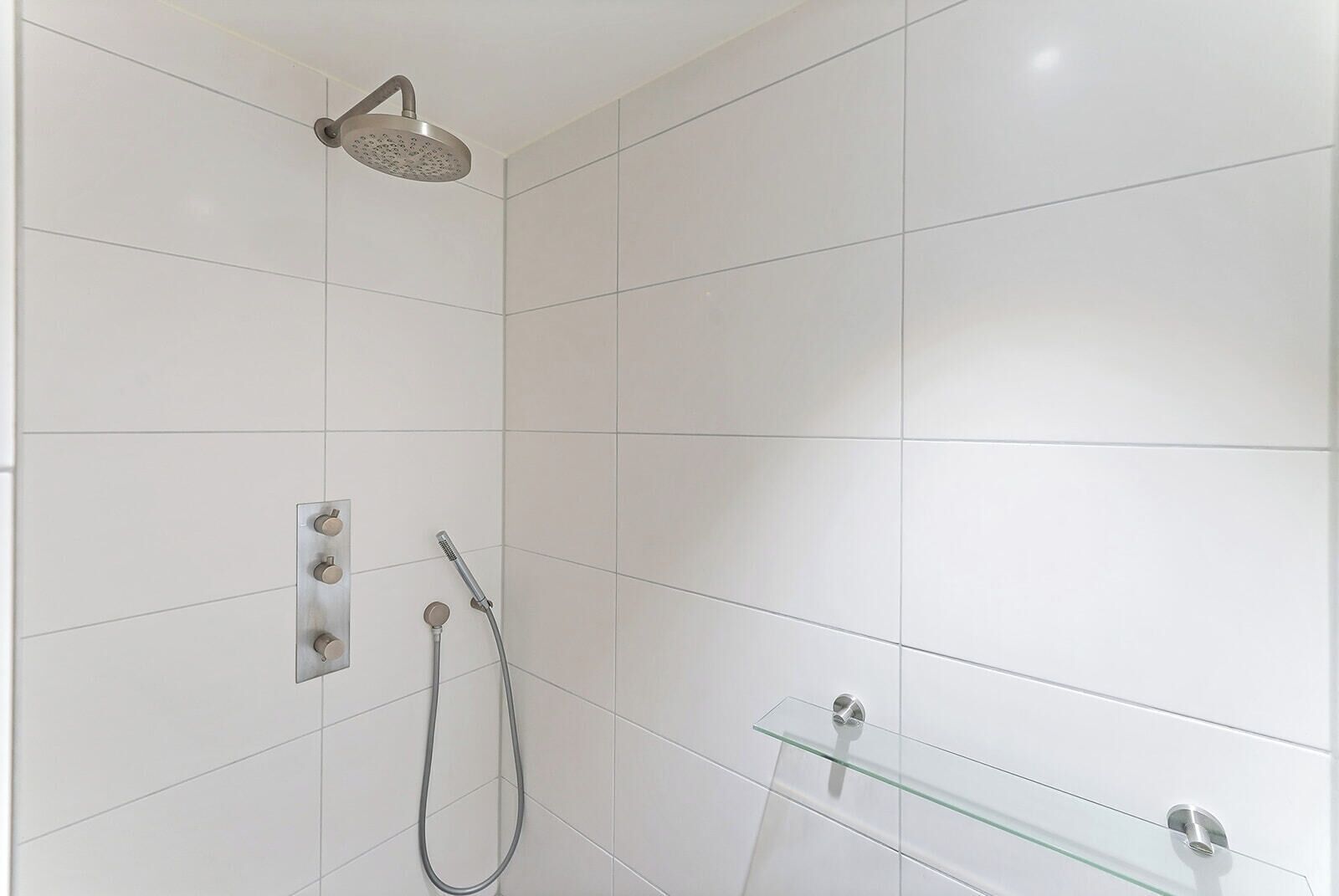 A modern shower with a handheld showerhead and a wall-mounted control panel.