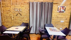 A room with bamboo walls, two tables with chess sets, and badminton rackets hanging on the wall. - Bamboo Junction Resort (Tehri)