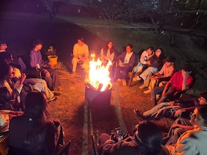 Un groupe de personnes assises en cercle autour d’un feu de camp, dans un cadre extérieur.