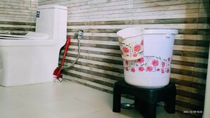 A bathroom with a toilet, bidet, and a bucket on a stool. - Bamboo Junction Resort (Tehri)