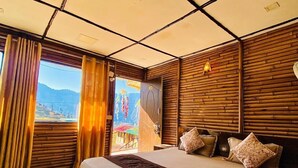 A modern bedroom with a large bed, wooden panel walls, and a view of a mountainous landscape through the window. - Bamboo Junction Resort (Tehri)