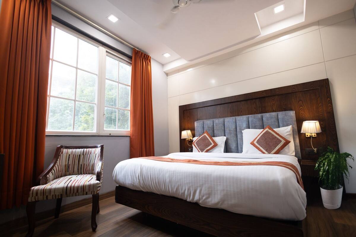 A hotel room with a large bed, a chair, a window with curtains, and a plant.