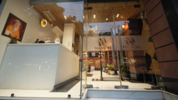 A modern interior with a reception desk, a staircase, and a sign for 'NAMOH'. - Hotel Namoh (New Delhi)