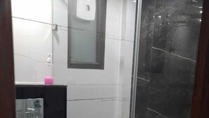 A bathroom with a toilet, a glass shower enclosure, a mirror, and a soap dispenser. - Hotel Namoh (New Delhi)