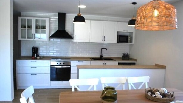 A modern kitchen with white cabinets, a wooden dining table, and pendant lighting.