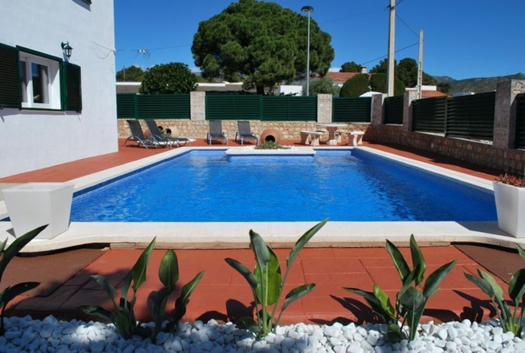 En swimmingpool med solstolar, en stenmur och ett stort träd i bakgrunden.