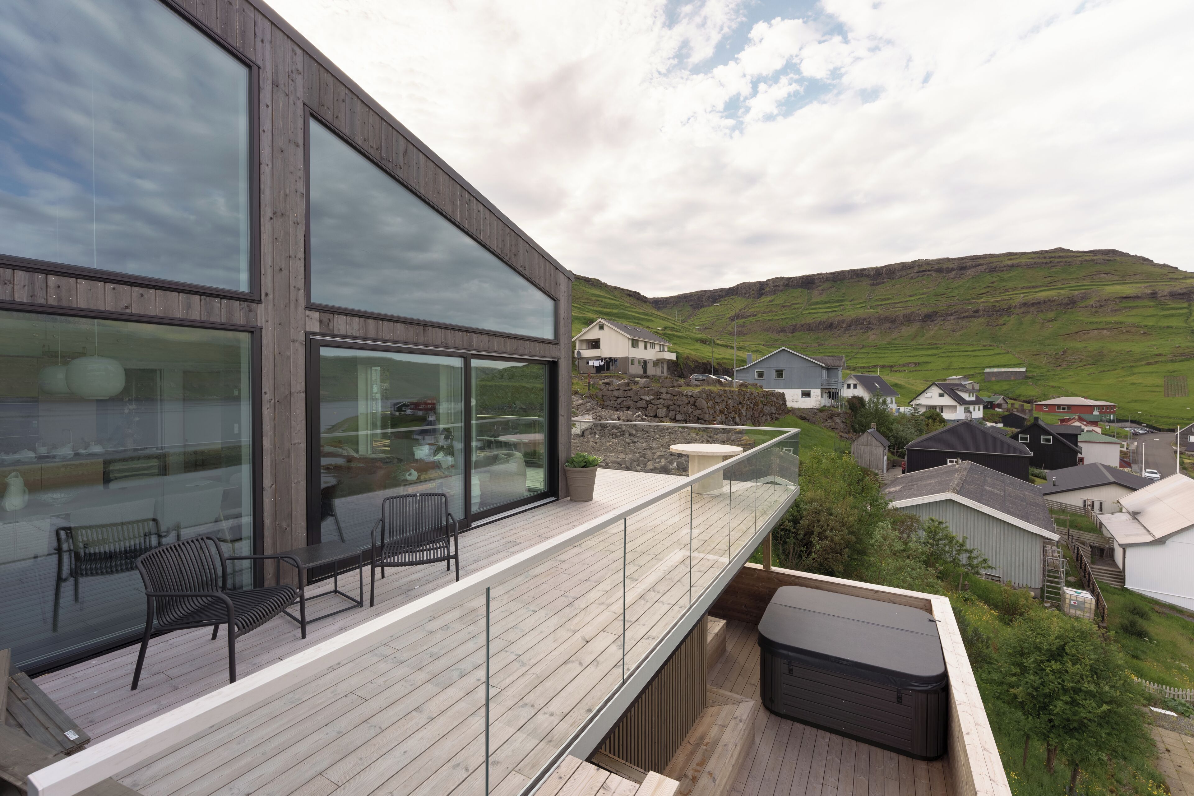 A modern building with large windows and a wooden deck with outdoor seating.