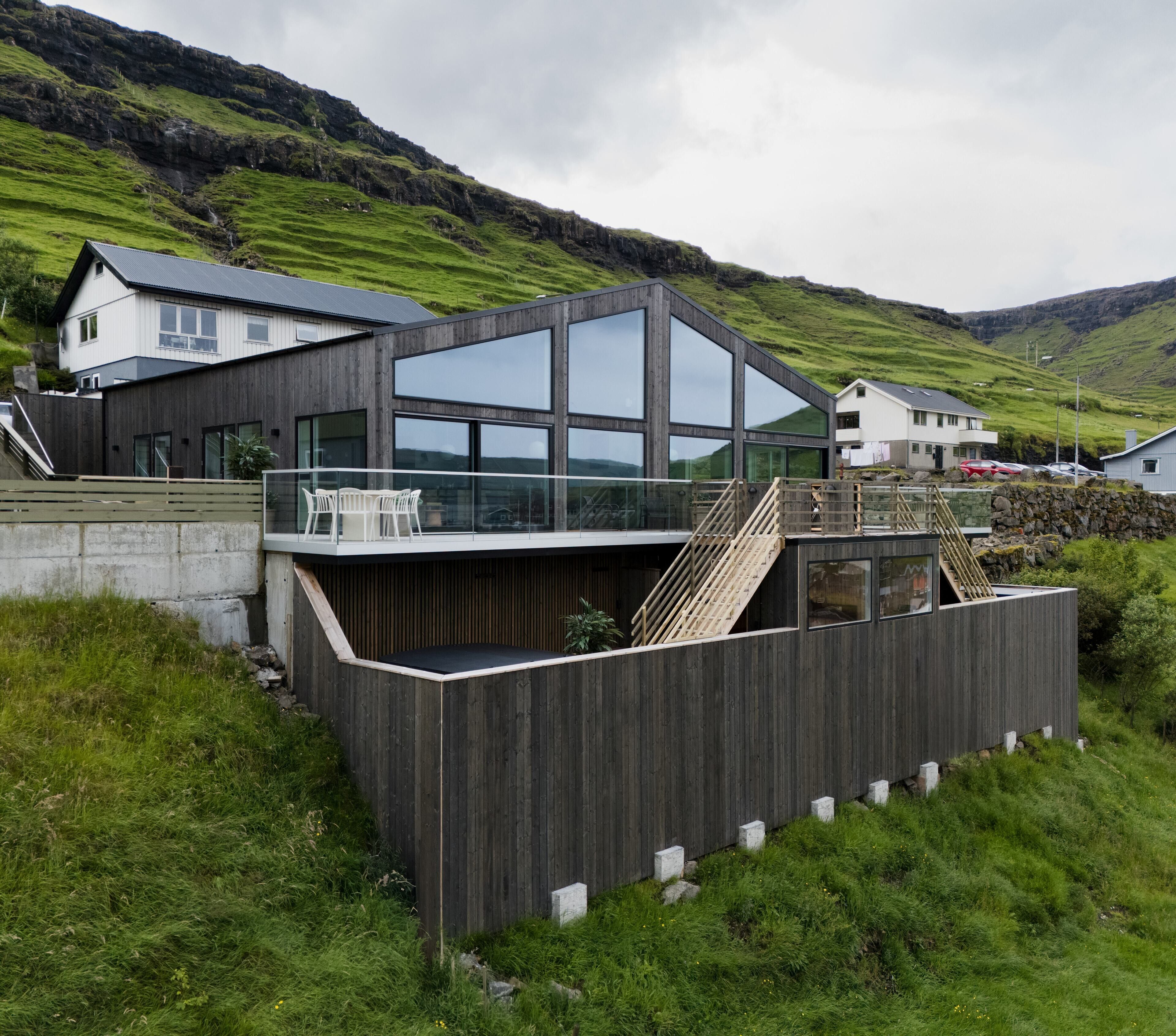A modern house with a large glass window, a wooden deck, and a stone wall.