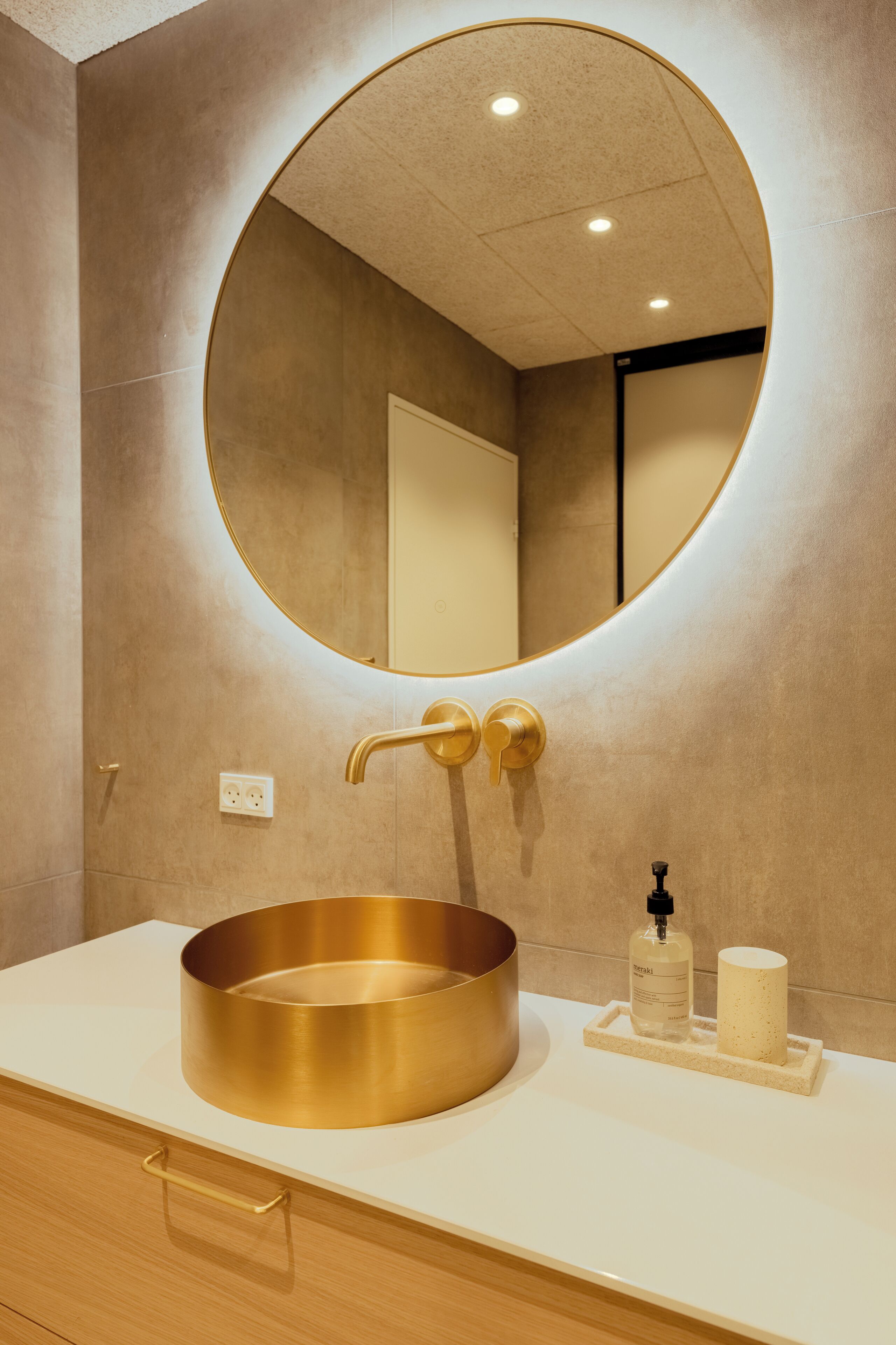 A bathroom with a round gold sink, a mirror, and a towel rack.