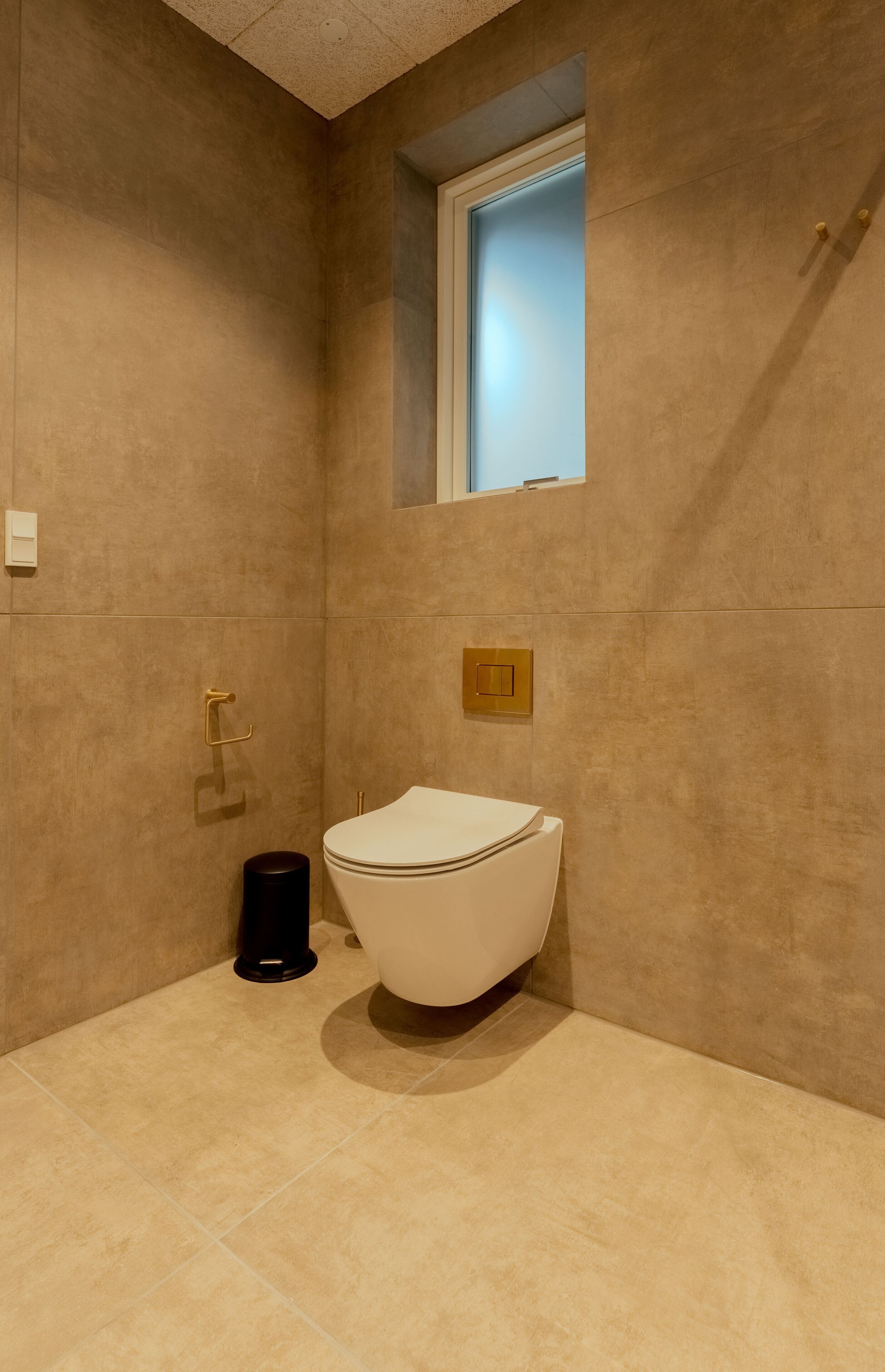Un baño moderno con inodoro blanco, una ventana pequeña y un perchero para toallas.