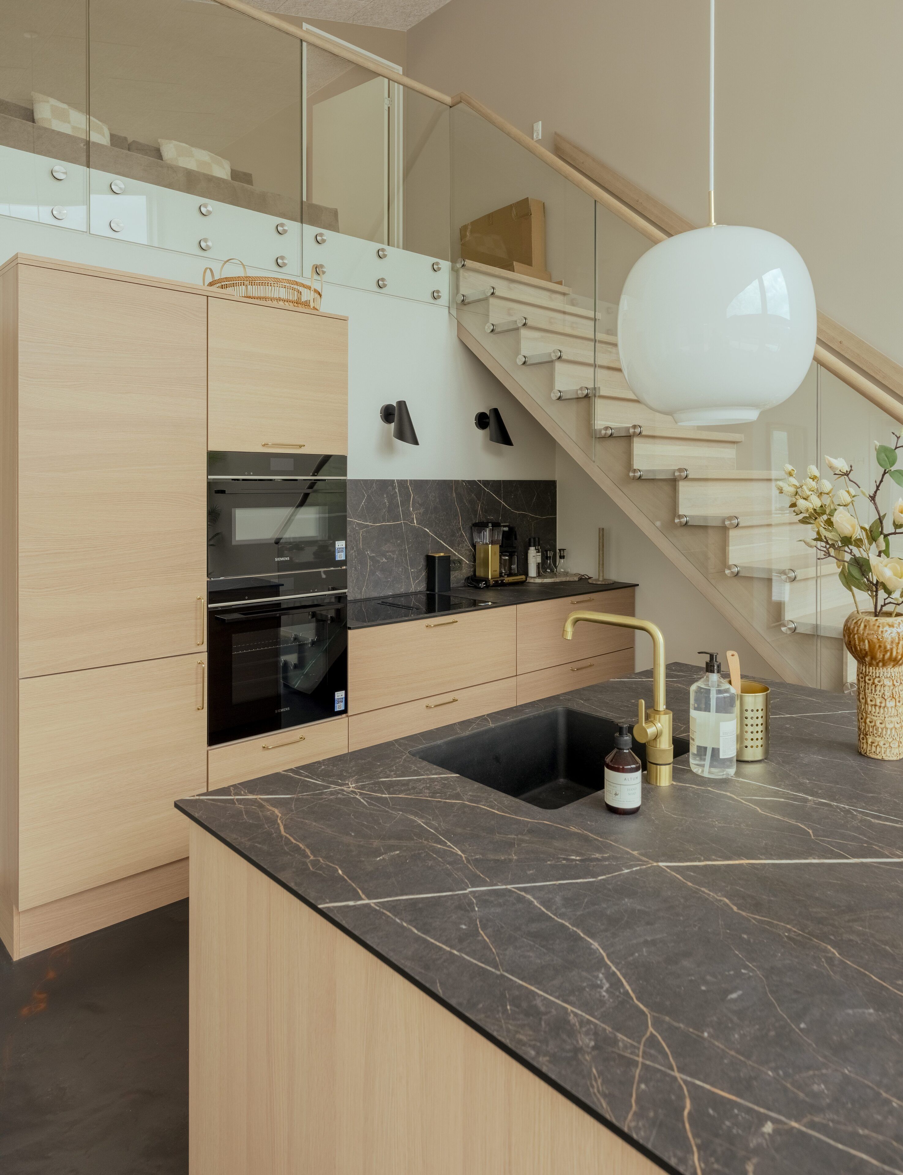 Eine moderne Küche mit schwarzem Marmor-Arbeitsplatz, Edelstahlgeräten und einer Holztreppe.